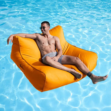 Man relaxing on an orange floating bean bag chair in a pool