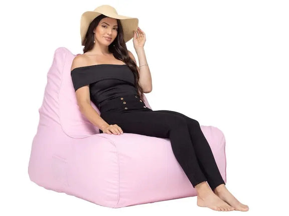 Woman sitting on a pink bean bag chair wearing a black outfit and beige hat.