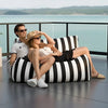 Two people sitting on a black and white striped bean bag chair with a scenic background.