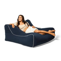 Woman lying on a navy blue bean bag chair with white piping on a white background