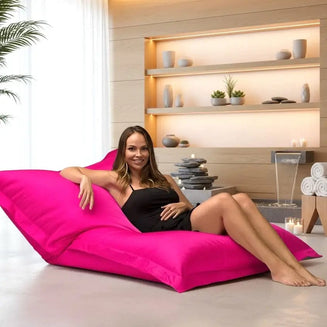 Woman sitting on a pink bean bag chair in a spa-like setting with shelves and plants.