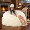 Young girl sitting on a fluffy white bean bag chair in a cozy room with a fireplace.