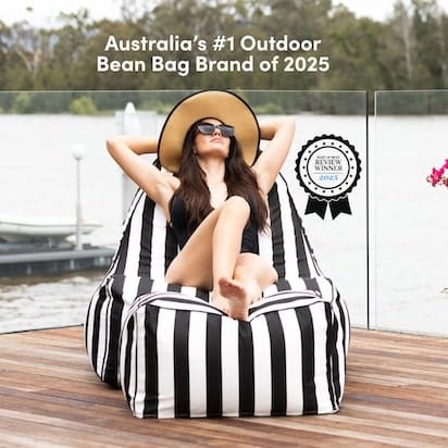 Woman relaxing on a black and white striped bean bag by a lake, with text about Australia's #1 Outdoor Bean Bag Brand of 2025.